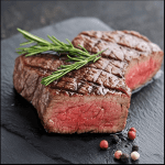 Juicy grilled steak with rosemary on a black slate, representing tips on how to soften tough cooked meat effectively